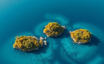 Aerial view of three uninhabited islands in ocean, showcasing serene waters and green vegetation under a clear sky.